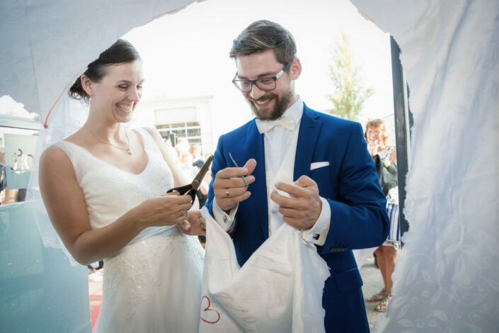 Brautpaar schneidet ein Herz aus einem Laken aus. Hochzeitsfotograf macht Hochzeitsbilder während der Hochzeitsfeier.