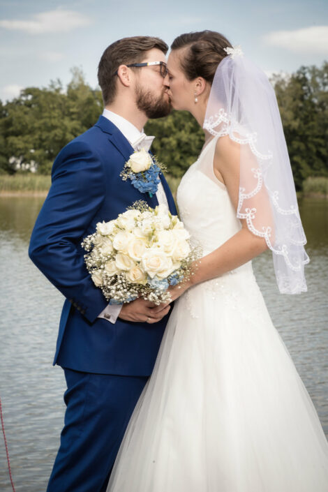 Brautpaar steht sich am Wasser gegenüber und küsst sich während des Brautpaarshootings in Falkensee