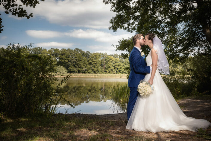Brautpaar steht sich am Wasser gegenüber und küsst sich während des Brautpaarshootings in Falkensee