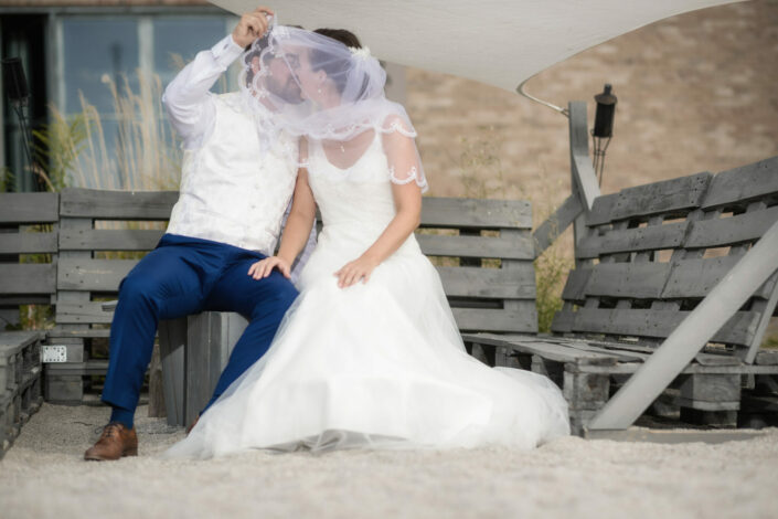 Brautpaar sitzt auf einer Bank und küsst sich während des Brautpaarshooting