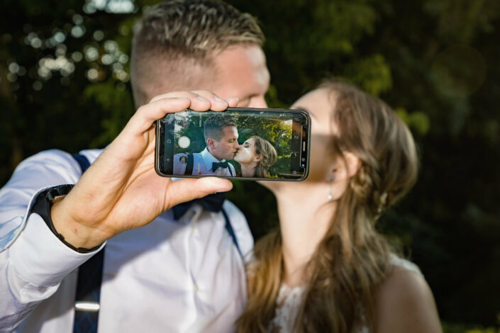 Authentische Hochzeitsbilder vom Hochzeitsfotograf Berlin:Bräutigam macht ein Selfie mit seiner Braut, der Hochzeitsfotograf fotografiert das Display und das Brautpaar in der Unschärfe